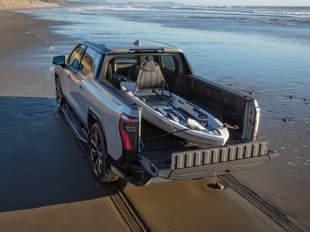 The GMC Sierra EV Pickup Truck Driving Down the Beach with a Kayak in the Truck Bed