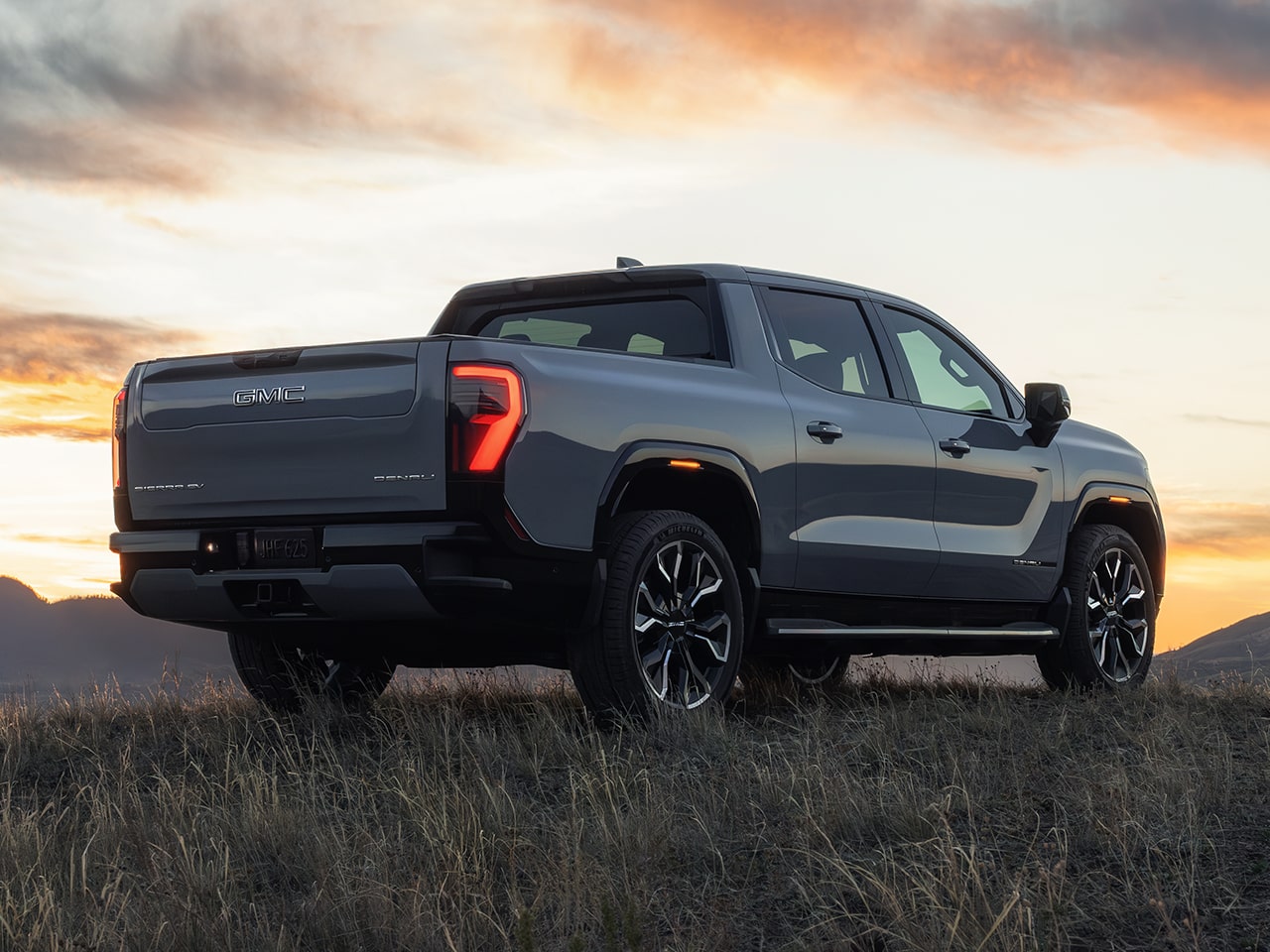 Rear Three-Quarter View of the GMC Sierra EV Pickup Truck as the Sun Sets Behind the Mountains